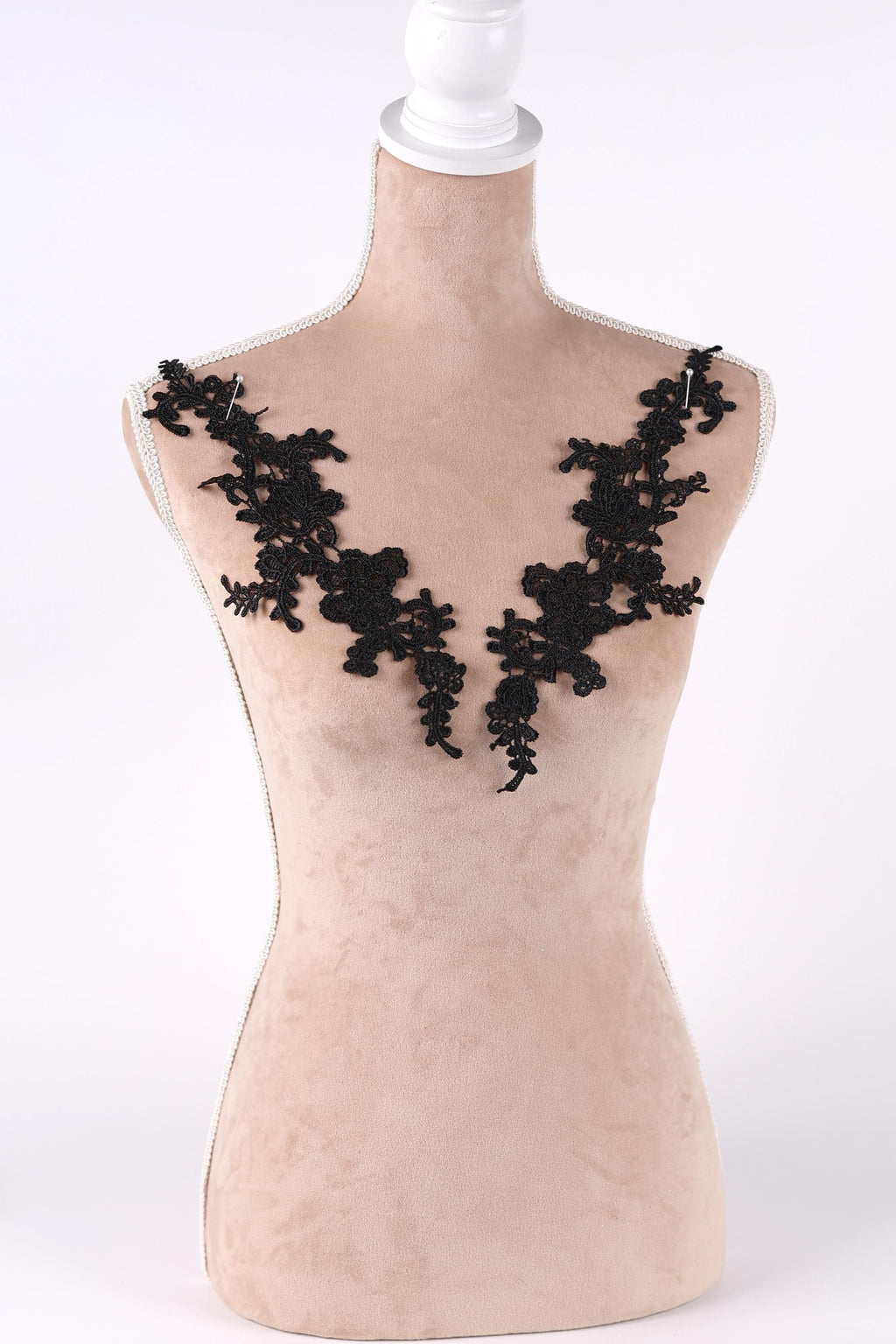A mannequin with a beige body and black lace or floral embroidery on the shoulders.