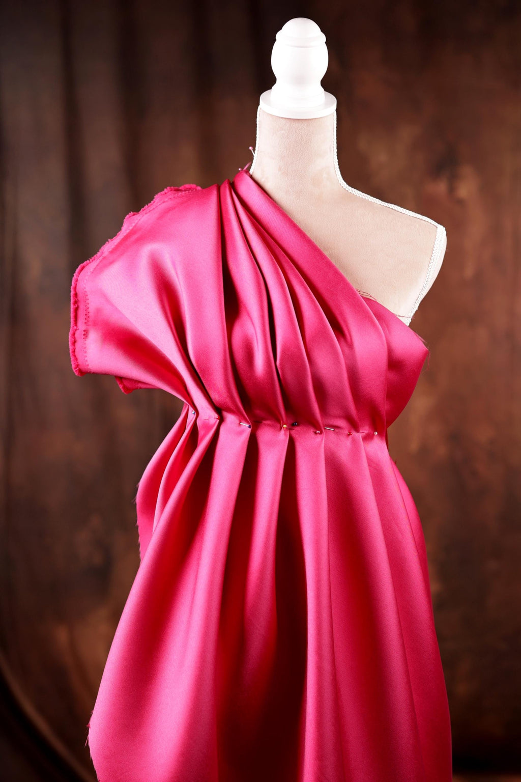 A mannequin wearing a vibrant red one-shoulder dress with a draped, flowing silhouette.