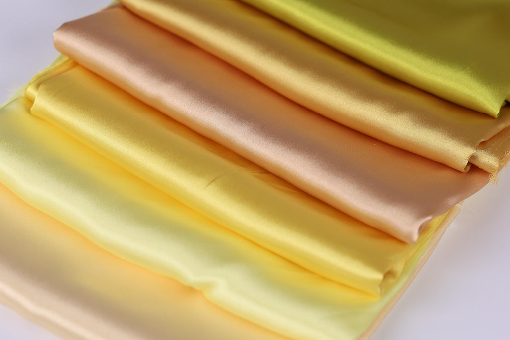 A close-up image of a stack of colorful fabric swatches, including yellow, orange, and green, arranged in a visually appealing manner.