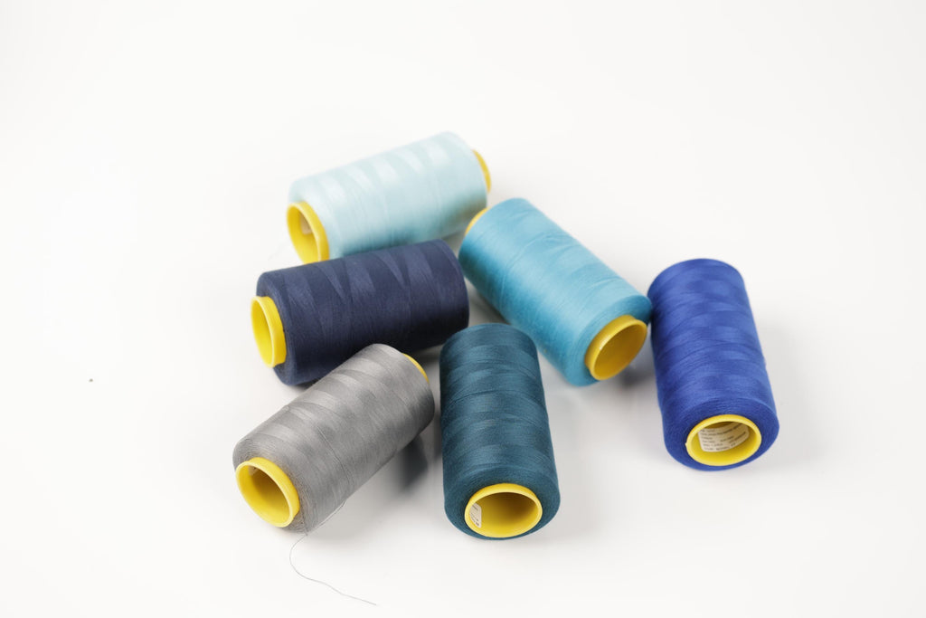 A collection of six spools of thread in various colors, including blue, gray, and yellow, arranged on a white background.