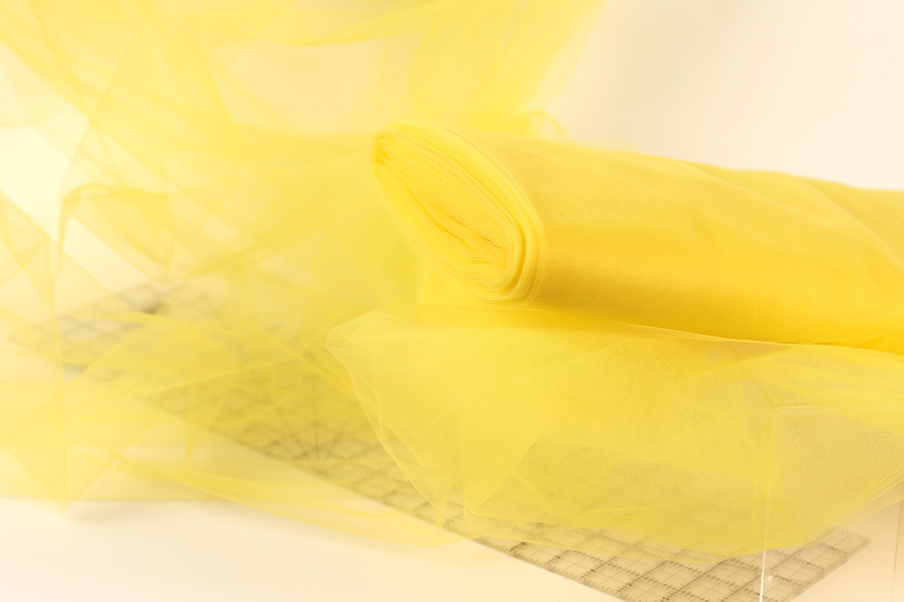 a close-up view of a yellow fabric, possibly tulle, with a blurred background.