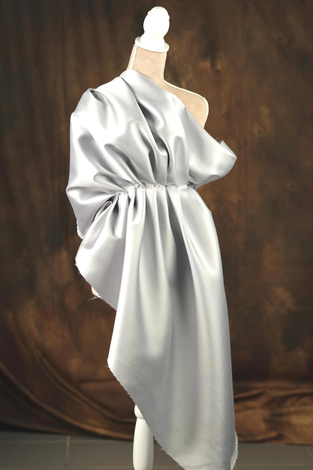 A mannequin wearing a gray satin dress with a draped, flowing design.