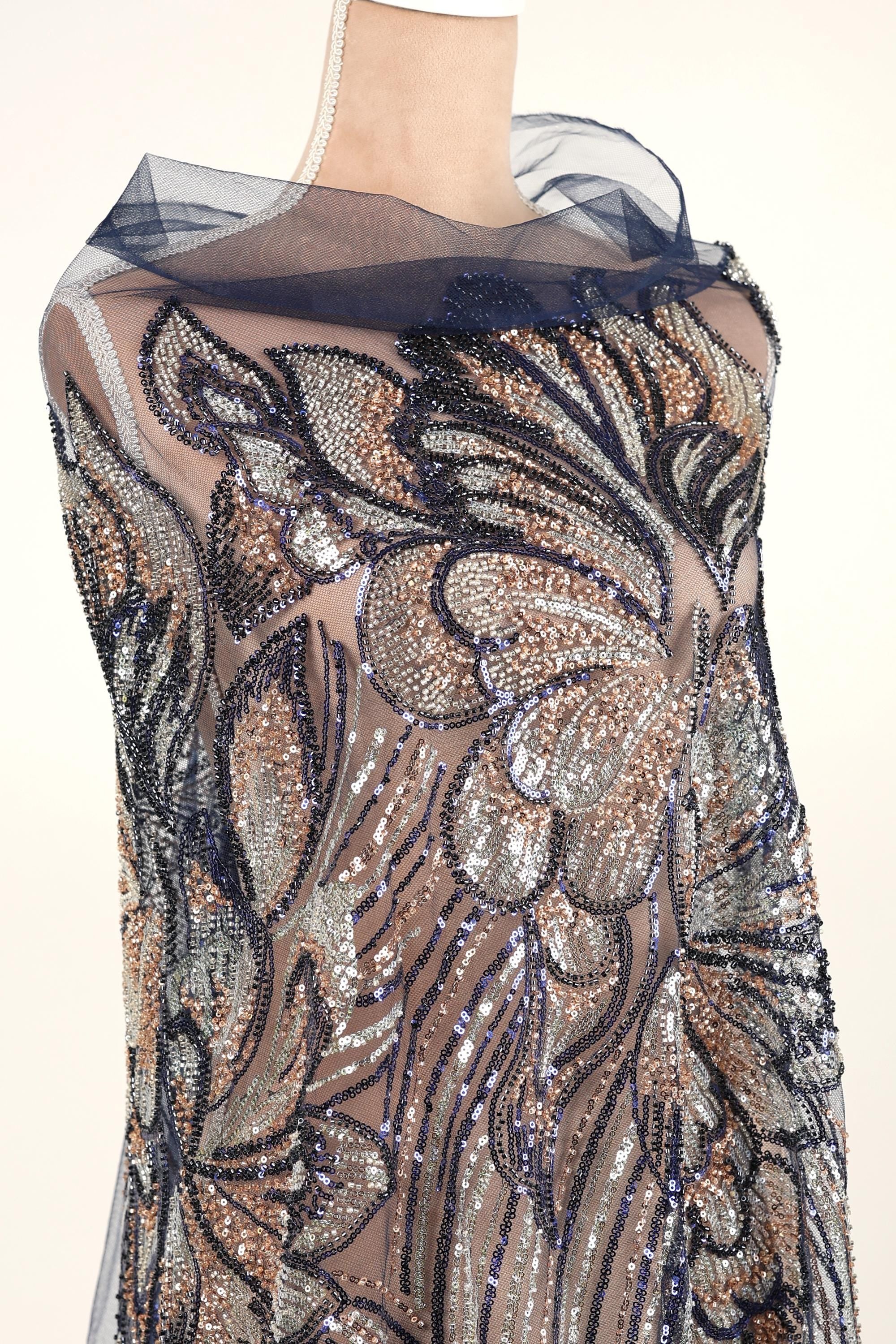 a mannequin wearing a dress with a sheer, sheer-like fabric that is covered in a floral pattern. The dress appears to be made of sequins and has a blue and black color scheme.