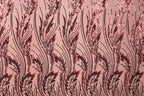 a close-up view of a fabric with a repeating pattern of red and black sequin designs. The pattern consists of long, thin lines that create a repeating floral or leaf-like design. The fabric appears to be a pinkish-red color, and the sequin designs are visible throughout the entire image.
