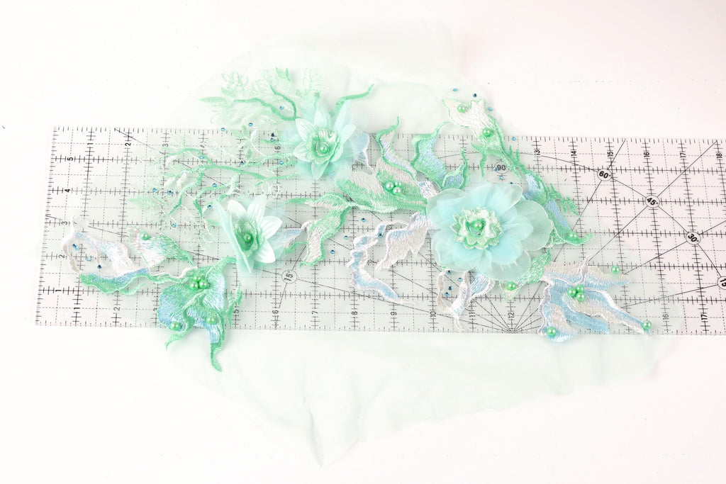 a collection of green and white floral embroidery pieces, including flowers and leaves, arranged on a ruler for scale.