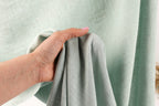 A hand is holding a light green fabric, possibly a curtain or textile, in front of a light green background.