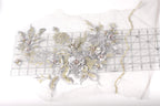 a close-up view of a delicate floral embroidery design on a white background. The design is composed of various silver and gold metallic flowers and leaves, creating a visually appealing and intricate pattern. The flowers are arranged in a way that they appear to be growing out of a transparent fabric, adding depth and dimension to the image. The precise placement of the flowers and leaves suggests a high level of craftsmanship and attention to detail.