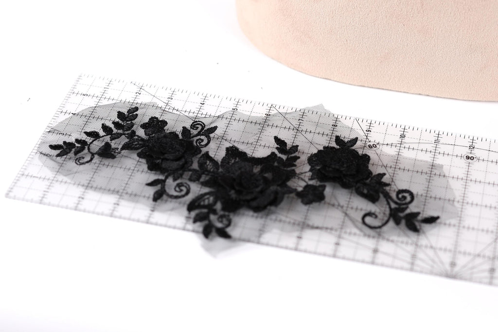 a transparent lace piece with black floral designs, placed on a ruler for scale.