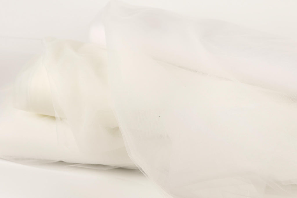 The image is a close-up of a white fabric, possibly a sheer or sheer-like material, with a soft, flowing texture.