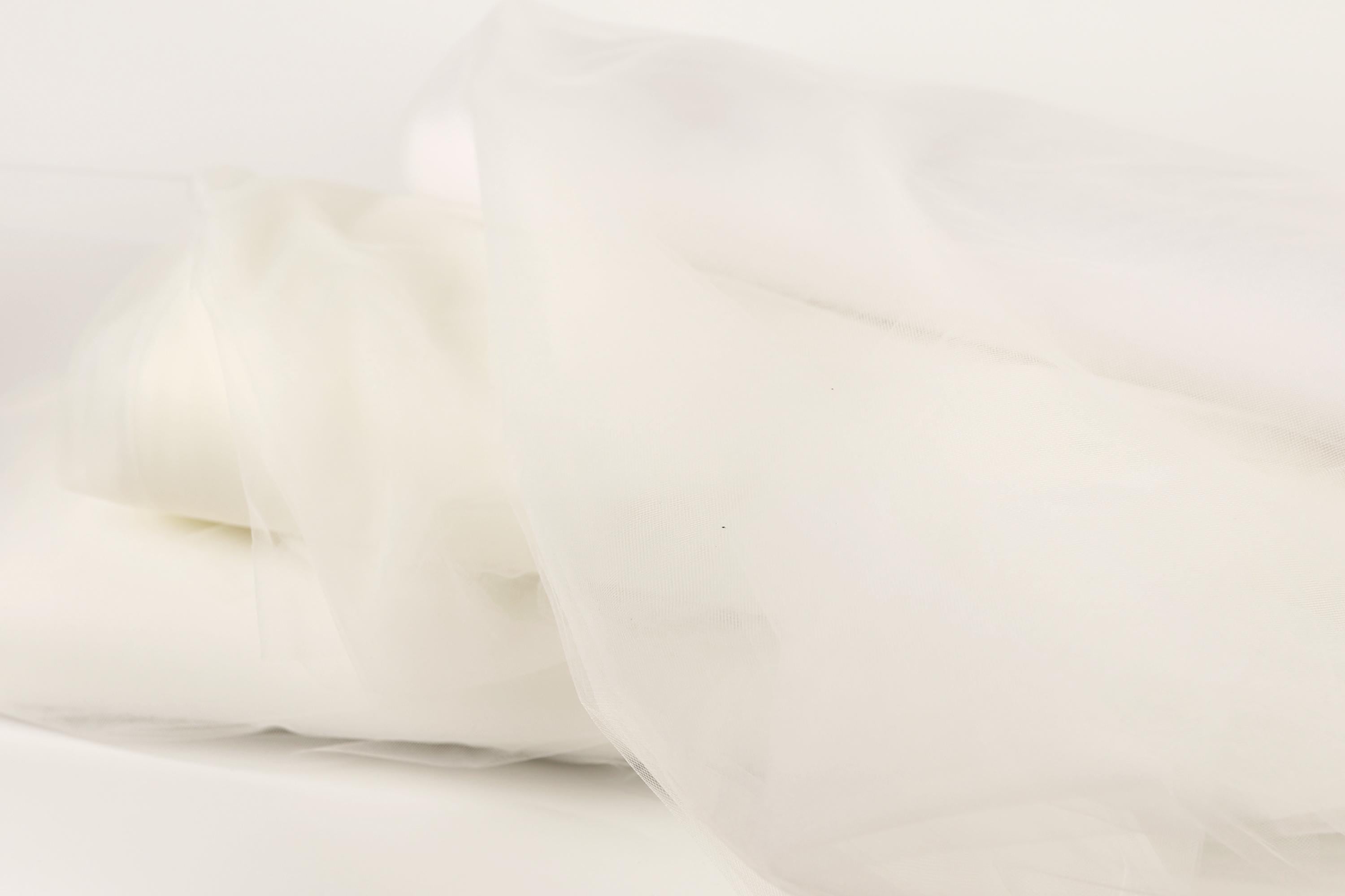 The image is a close-up of a white fabric, possibly a sheer or sheer-like material, with a soft, flowing texture.