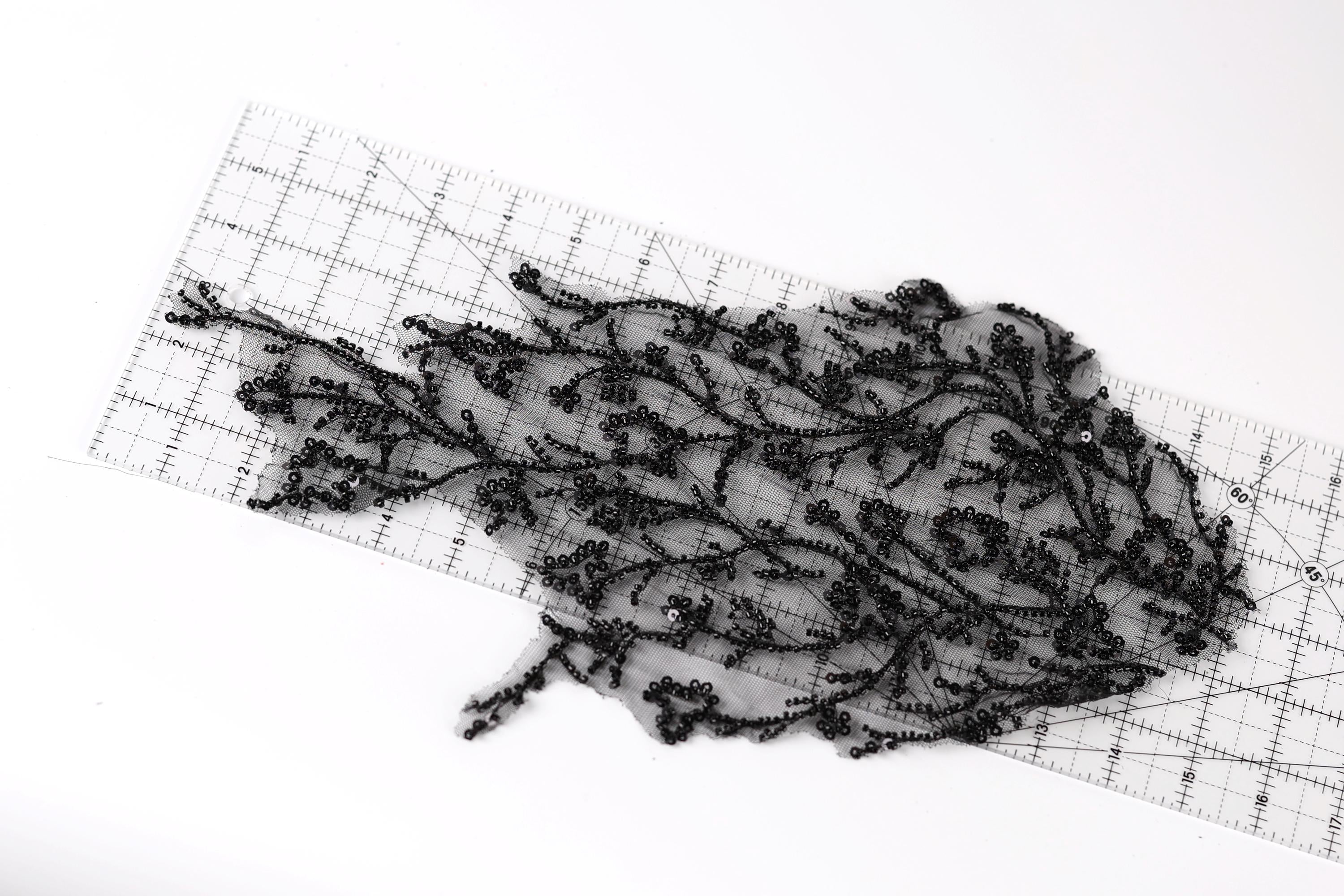 a piece of black lace with intricate patterns, laid out on a transparent ruler.