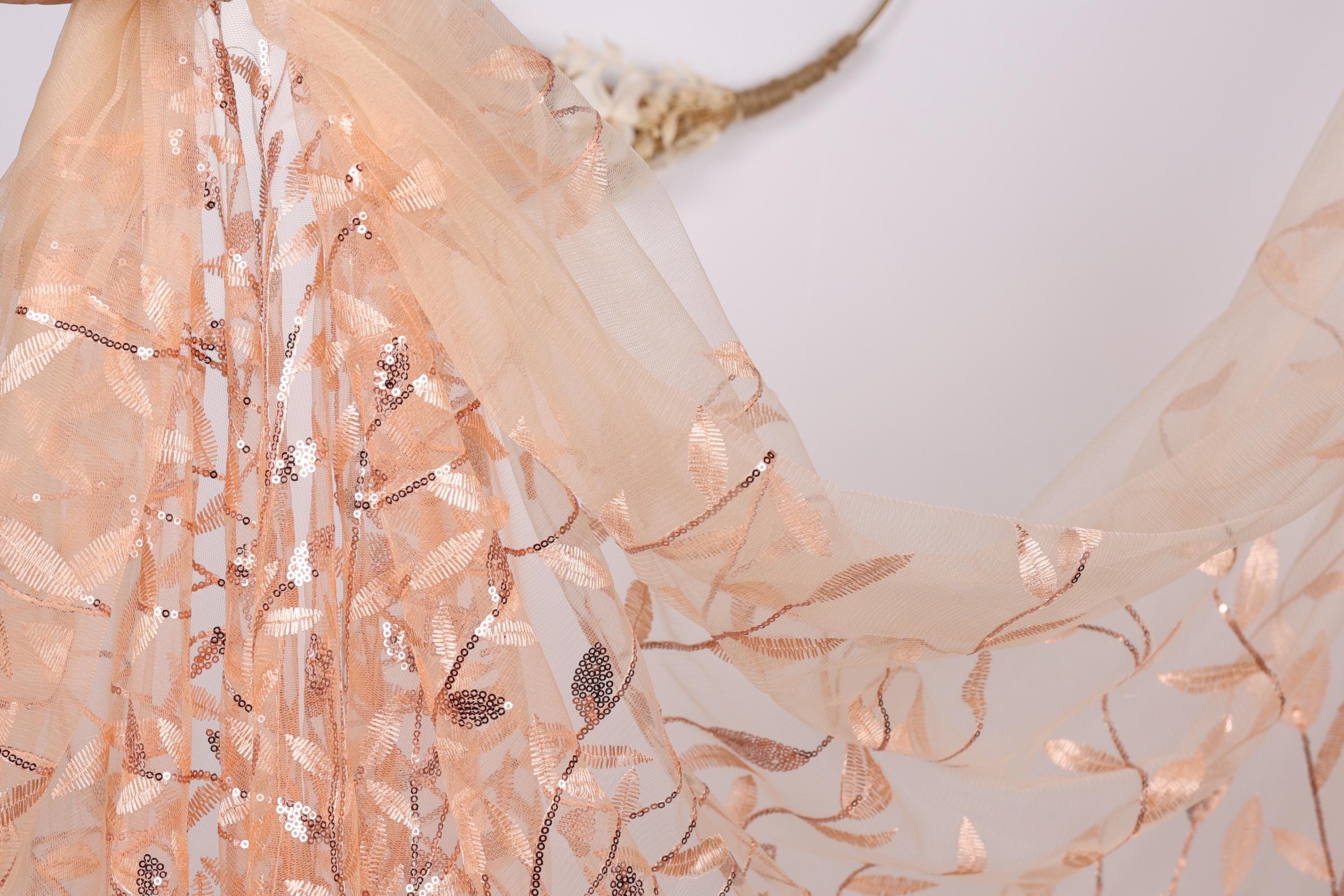 a delicate, peach-colored fabric with a floral pattern, including leaves and sequins. The fabric appears to be a sheer or sheer-like material, with a soft and delicate texture.