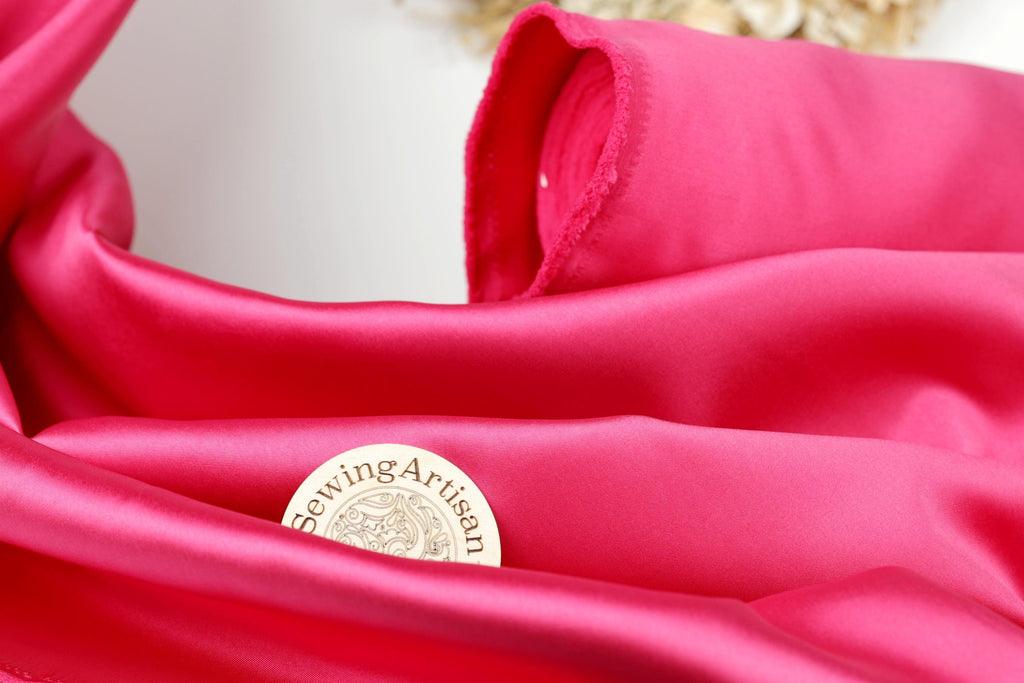 A close-up view of a bright pink fabric with a small white label that reads "SewingArtisan" placed on it.