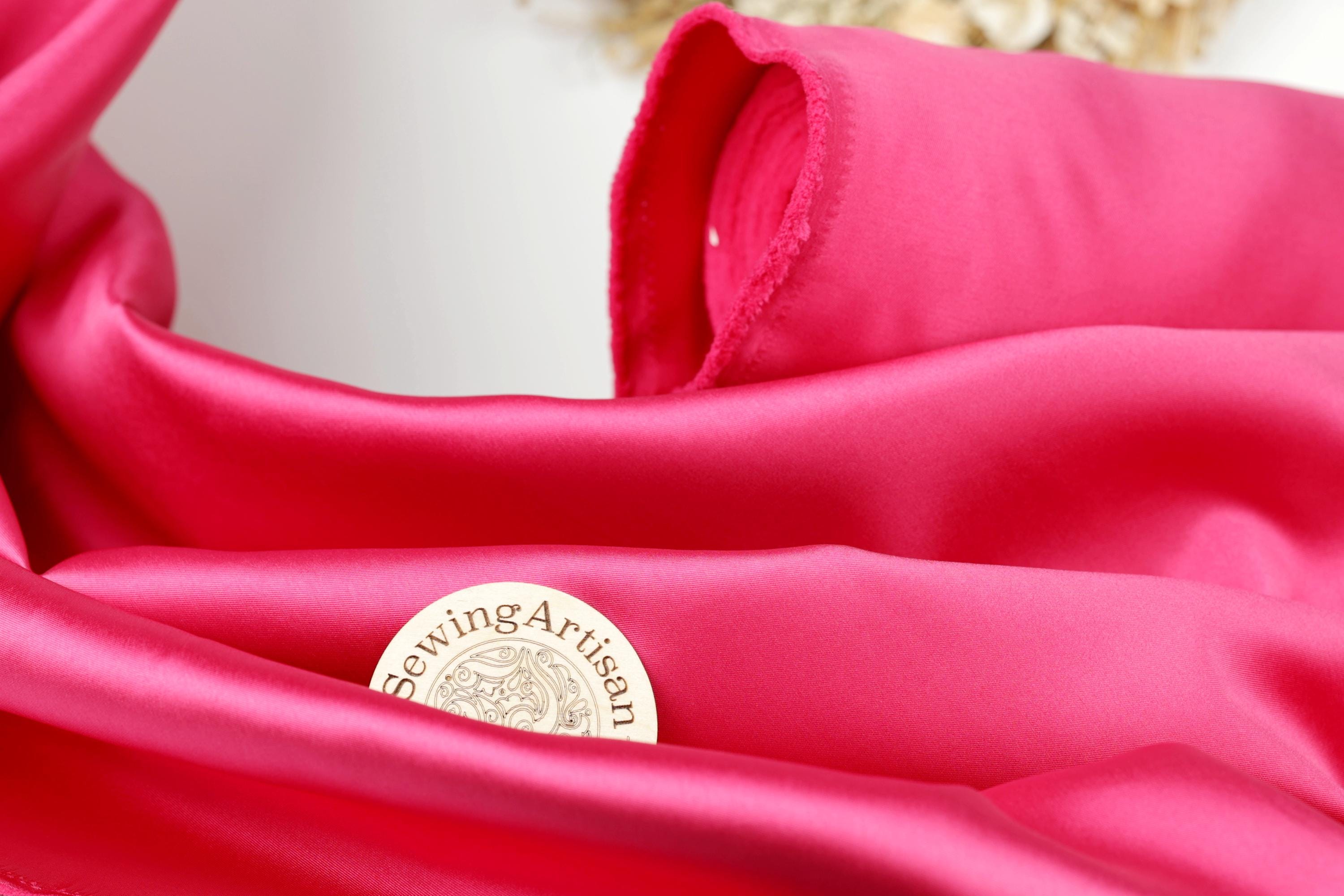 A close-up view of a bright pink fabric with a small white label that reads "SewingArtisan" placed on it.