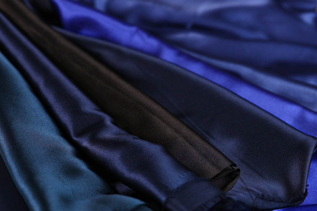 A close-up view of a variety of colorful satin fabric, including shades of blue, black, and brown, arranged in a visually appealing manner.