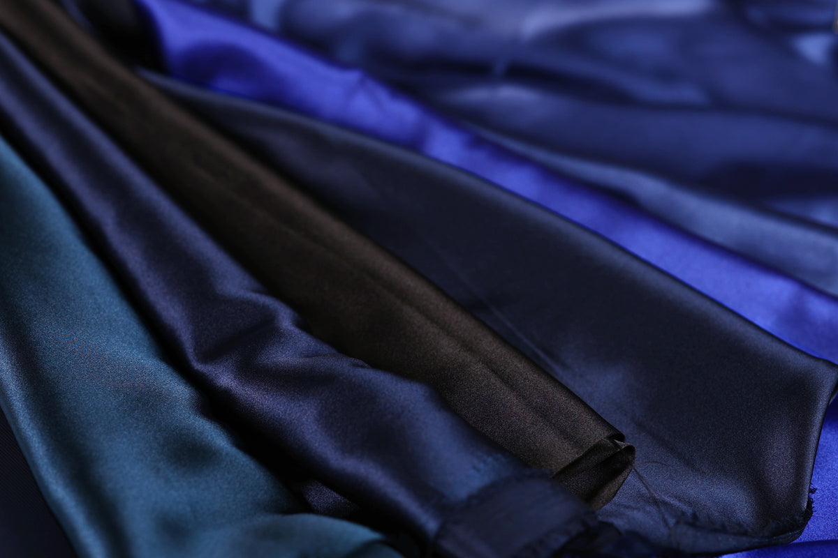 A close-up view of a variety of colorful satin fabric, including shades of blue, black, and brown, arranged in a visually appealing manner.