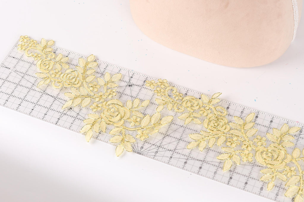a close-up view of a piece of fabric with a floral pattern, including yellow flowers and leaves, placed on a ruler.