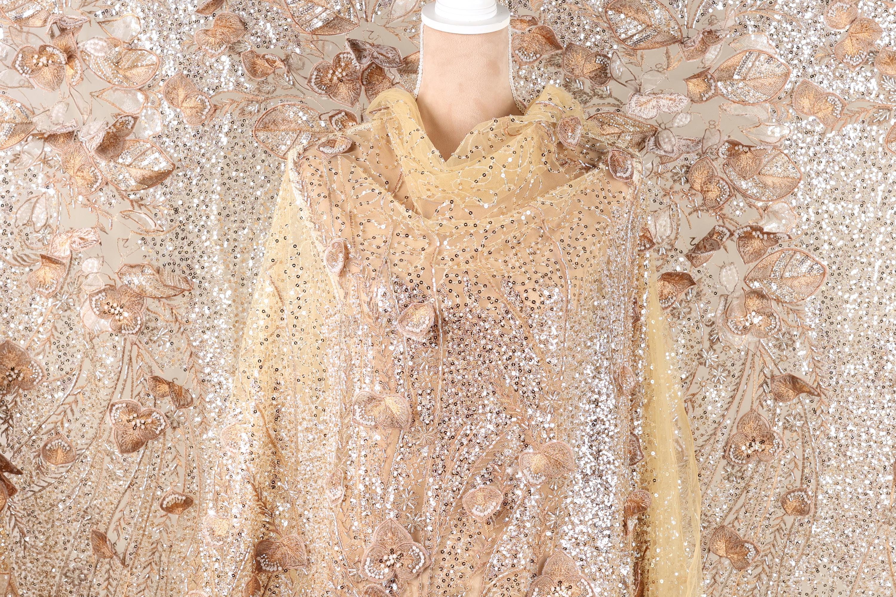 a mannequin wearing a gold and beige sequined dress with a floral pattern.