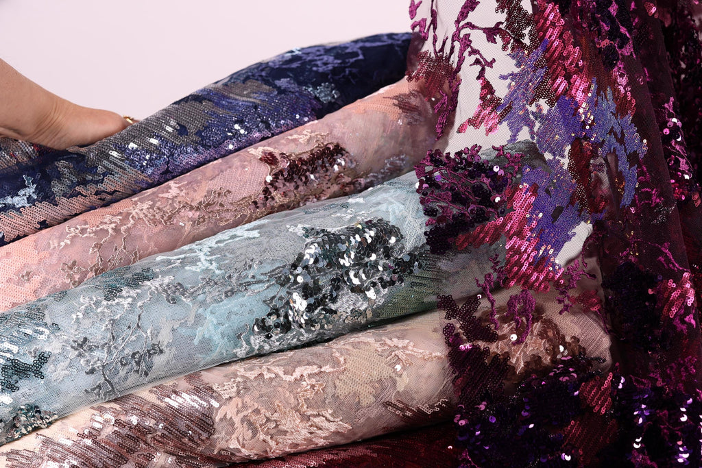 a close-up view of a pile of fabric with sequin designs, showcasing various shades of blue, pink, and purple.