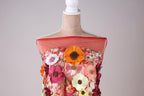 A mannequin wearing a red dress with a variety of colorful flowers and embroidery.