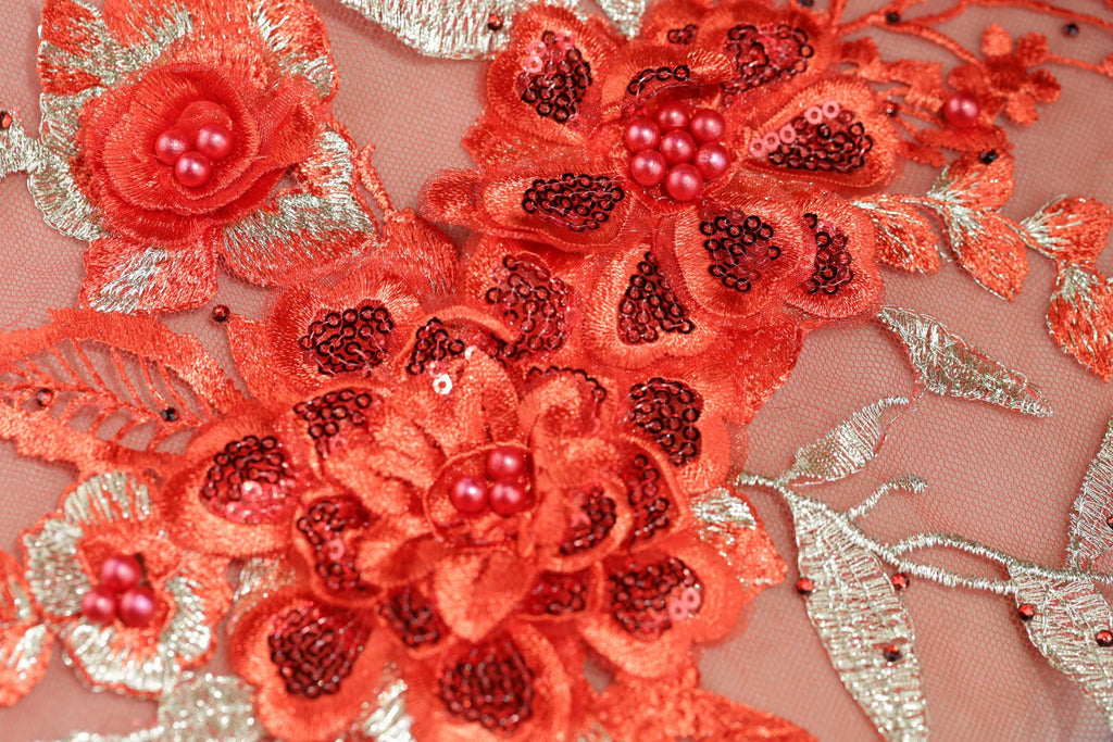 a close-up view of a delicate, intricately designed fabric with a floral pattern. The fabric is adorned with a variety of red and gold sequins, beads, and flowers, creating a visually striking and detailed design.