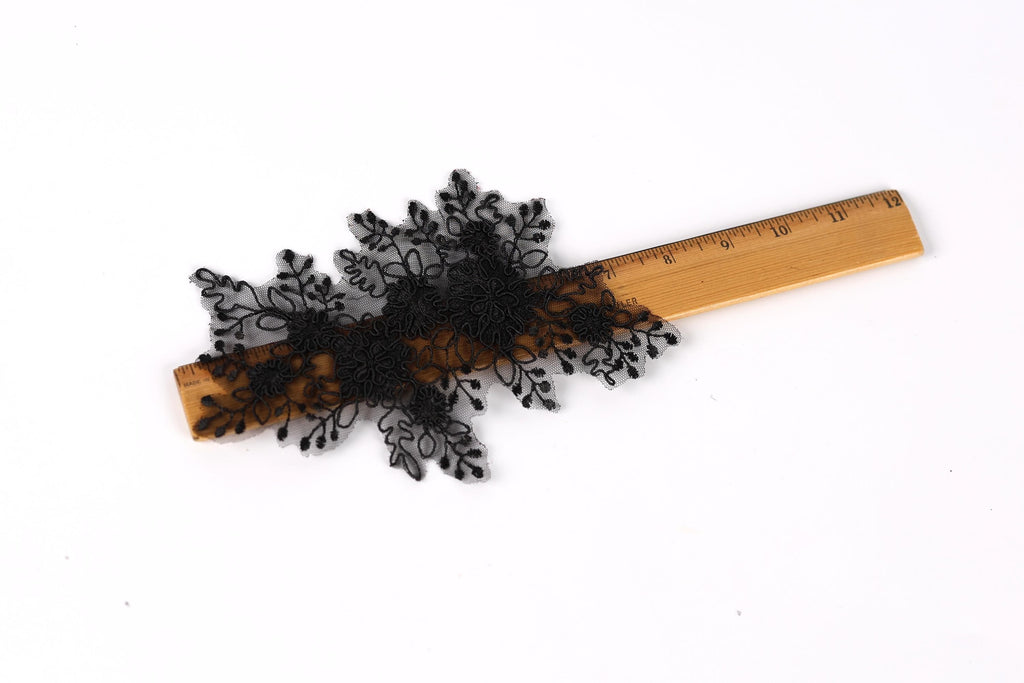 a wooden ruler with black lace or embroidery attached to it, placed on a white background.