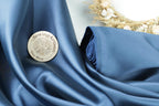 A round badge with the text "SewingArtisan Easy Shop" is placed on a blue fabric, with a wreath of dried flowers visible in the background.