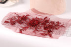 a close-up view of a red floral embroidery on a piece of fabric, with a pink fabric item in the background.