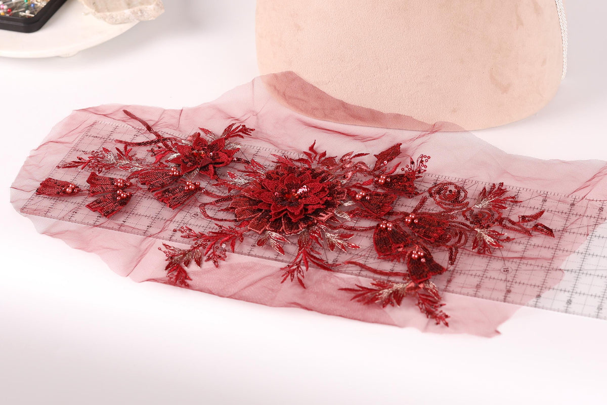 a close-up view of a red floral embroidery on a piece of fabric, with a pink fabric item in the background.