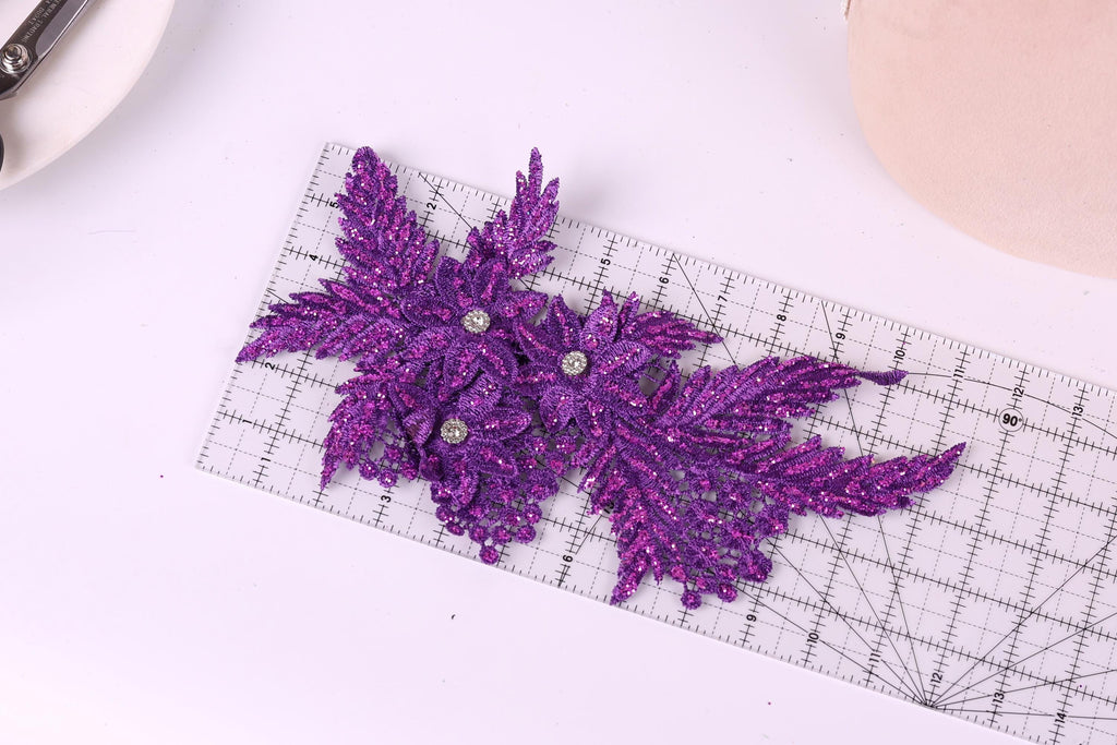 a pair of purple glitter leaves placed on a ruler, which is lying on a white surface.