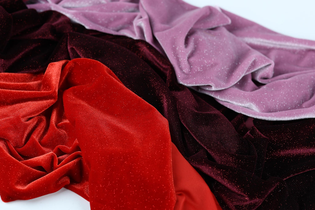 a close-up view of a pile of colorful velvet fabric, with a mix of red, purple, and black hues.