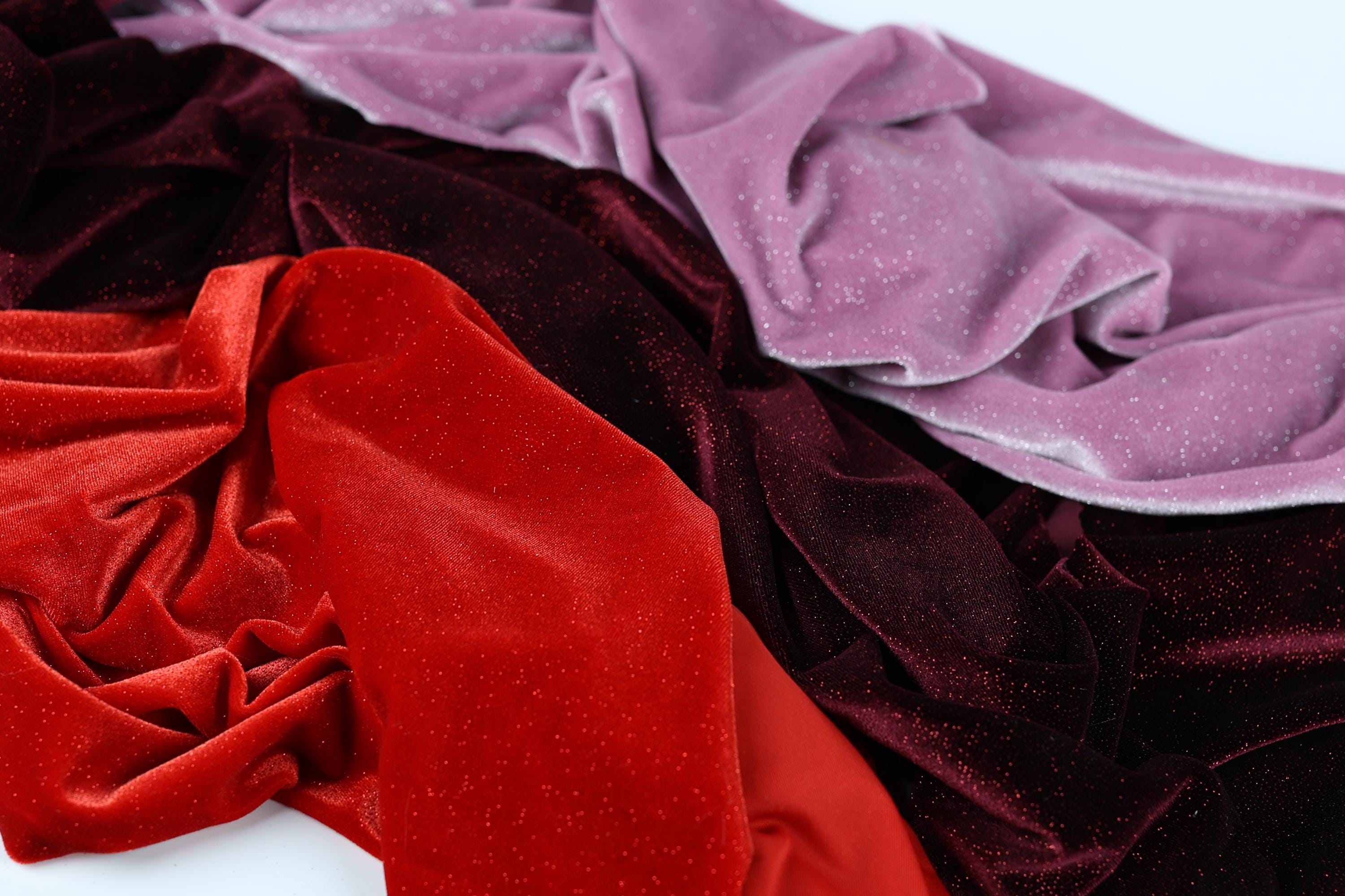 a close-up view of a pile of colorful velvet fabric, with a mix of red, purple, and black hues.