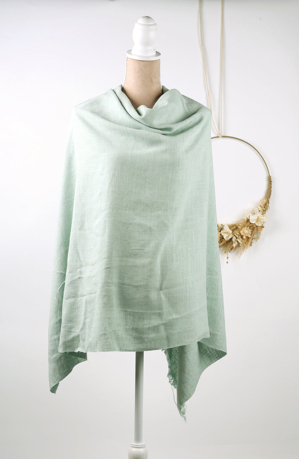 A light green shawl draped over a mannequin torso, displayed on a white mannequin stand.
