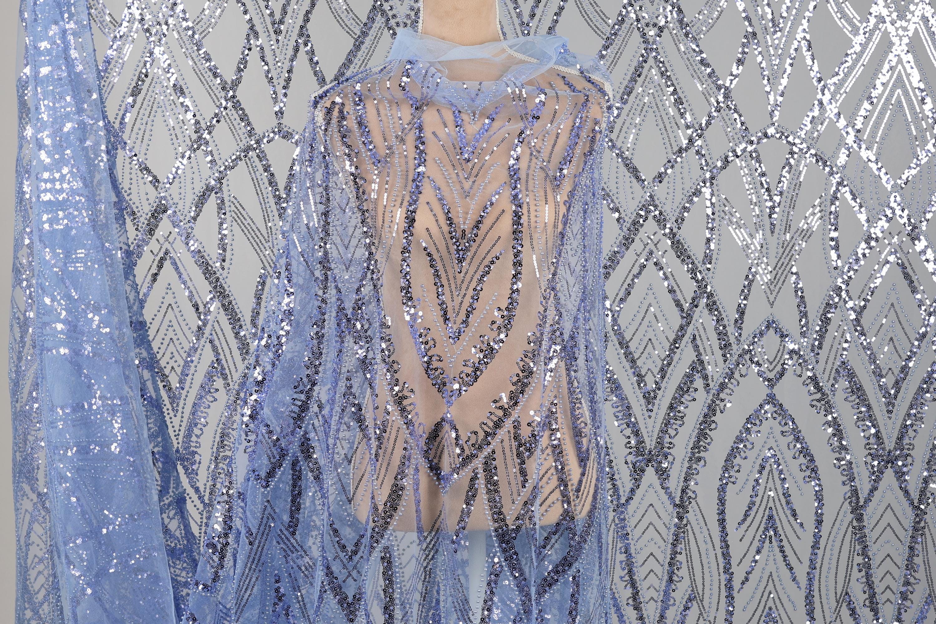 a sequin fabric with a blue and silver pattern, hanging against a gray background.