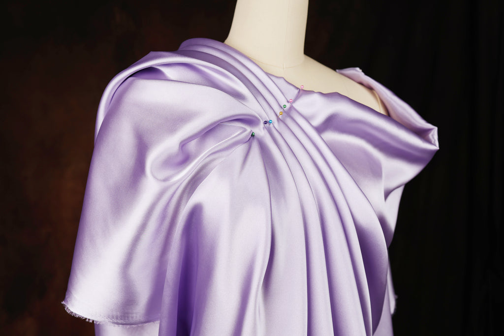 A mannequin wearing a lavender satin dress with a draped, flowing silhouette.