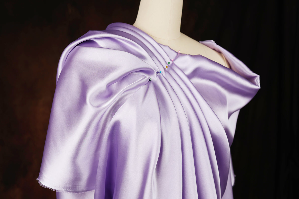 A mannequin wearing a lavender satin dress with a draped, flowing silhouette.