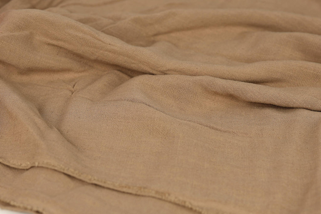 A close-up view of a crumpled, beige fabric, possibly a blanket or garment, with visible wrinkles and folds.