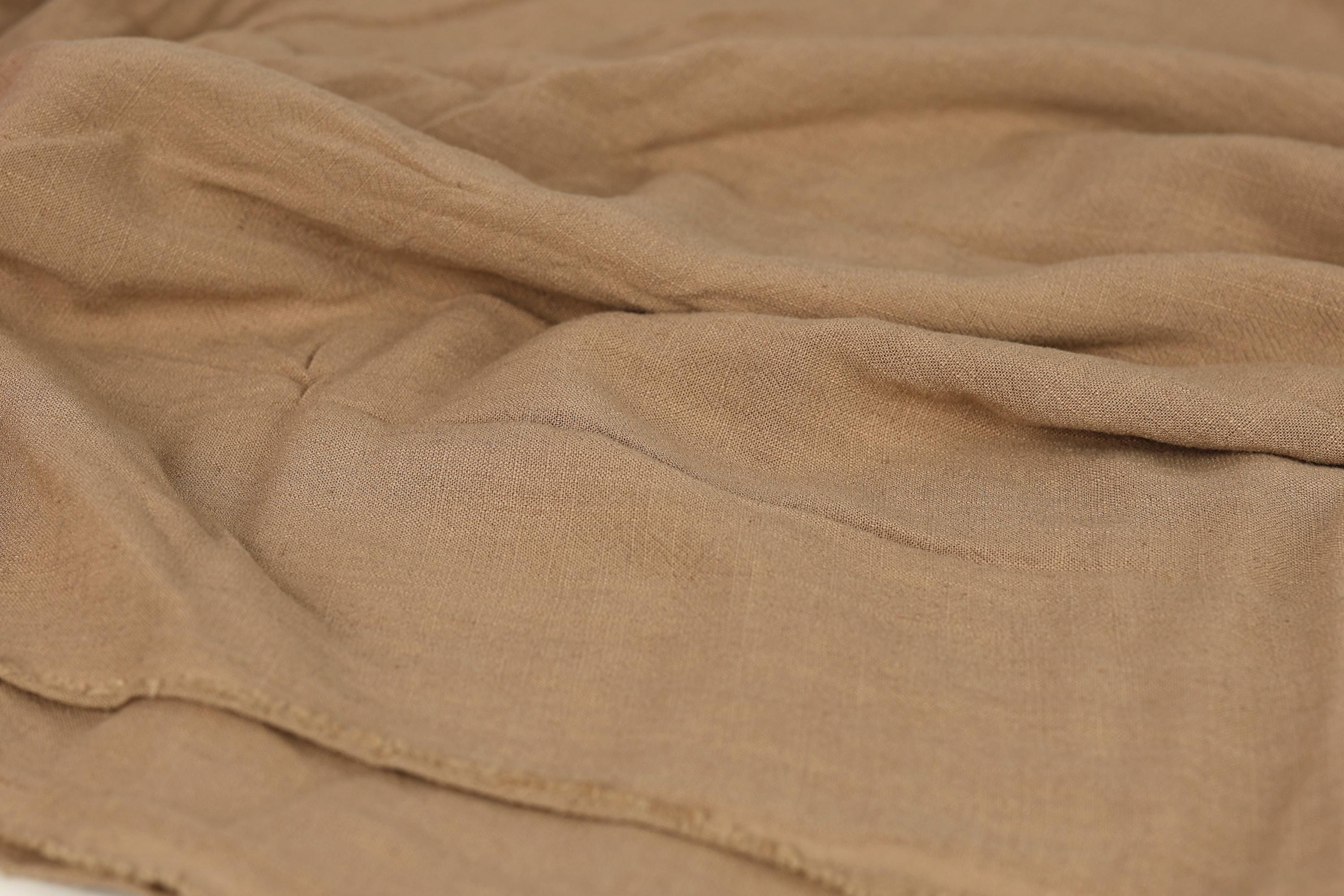 A close-up view of a crumpled, beige fabric, possibly a blanket or garment, with visible wrinkles and folds.
