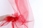 A hand is holding a piece of red tulle fabric, which appears to be a decorative material.
