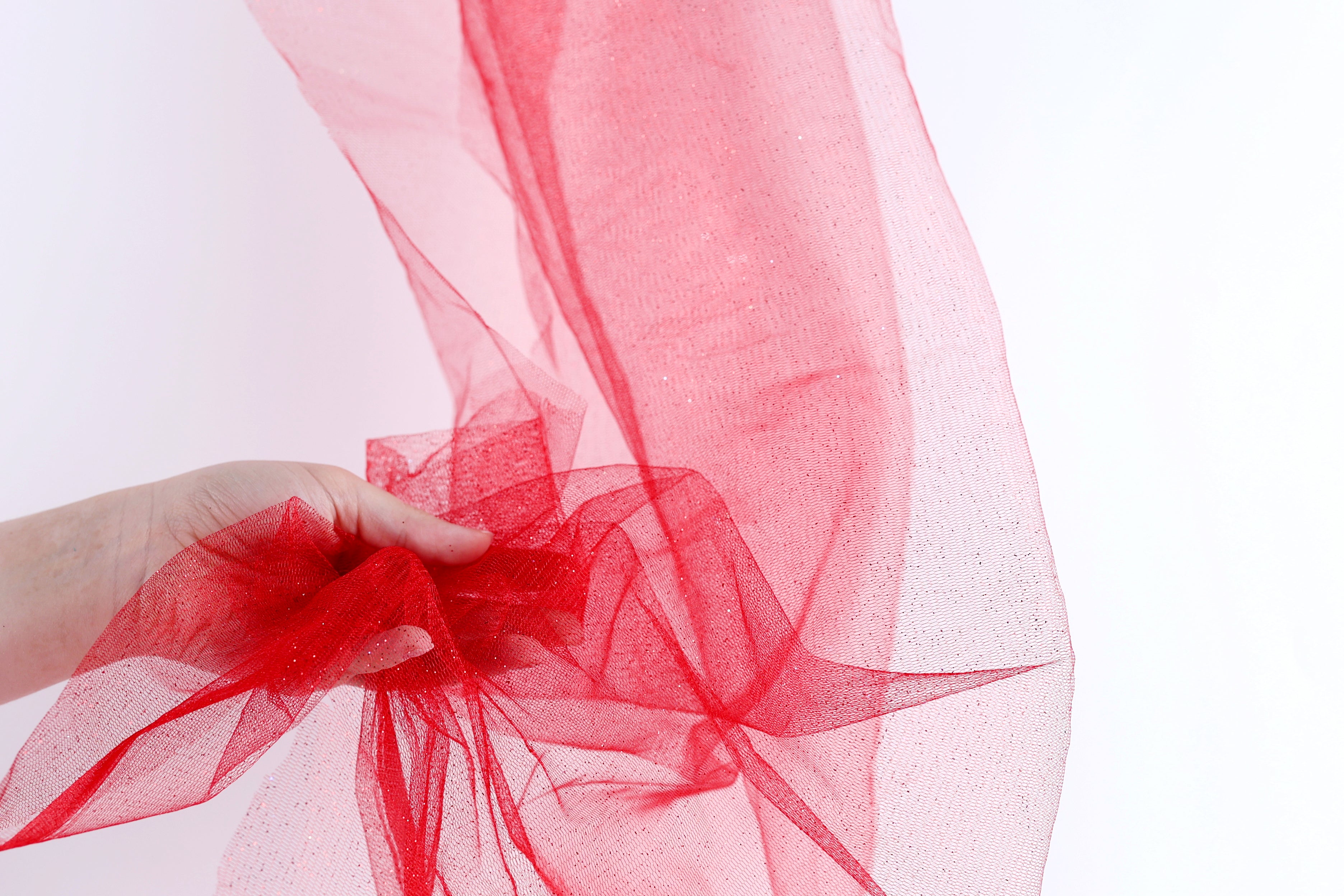 A hand is holding a piece of red tulle fabric, which appears to be a decorative material.
