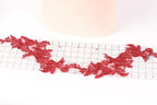 a red lace-like fabric with a floral pattern, placed on a ruler for scale.