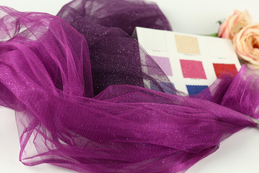 a close-up view of a purple glittery fabric, with a color swatch card displaying various fabric colors next to it.