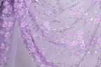 a close-up view of a fabric with a delicate floral pattern of purple roses and leaves. The fabric appears to be made of sheer material, allowing the intricate details of the flowers to be clearly visible. The overall color scheme of the fabric is a soft, pastel purple, which complements the delicate nature of the floral design.
