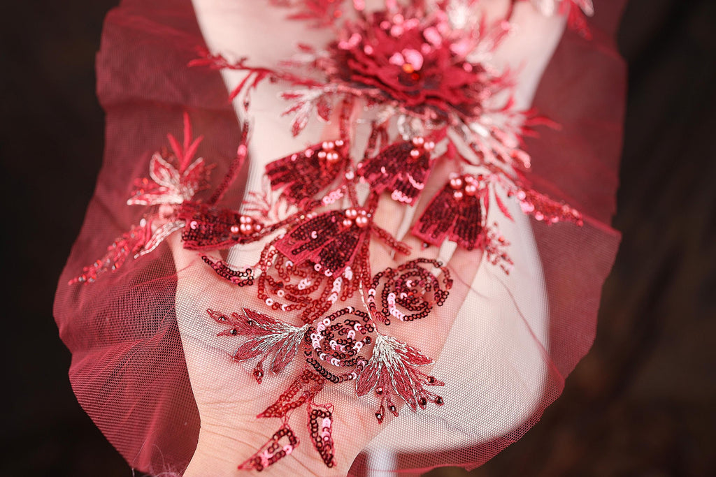 A close-up view of a hand adorned with a red and silver sequin design, featuring a floral pattern and a large flower-like element.