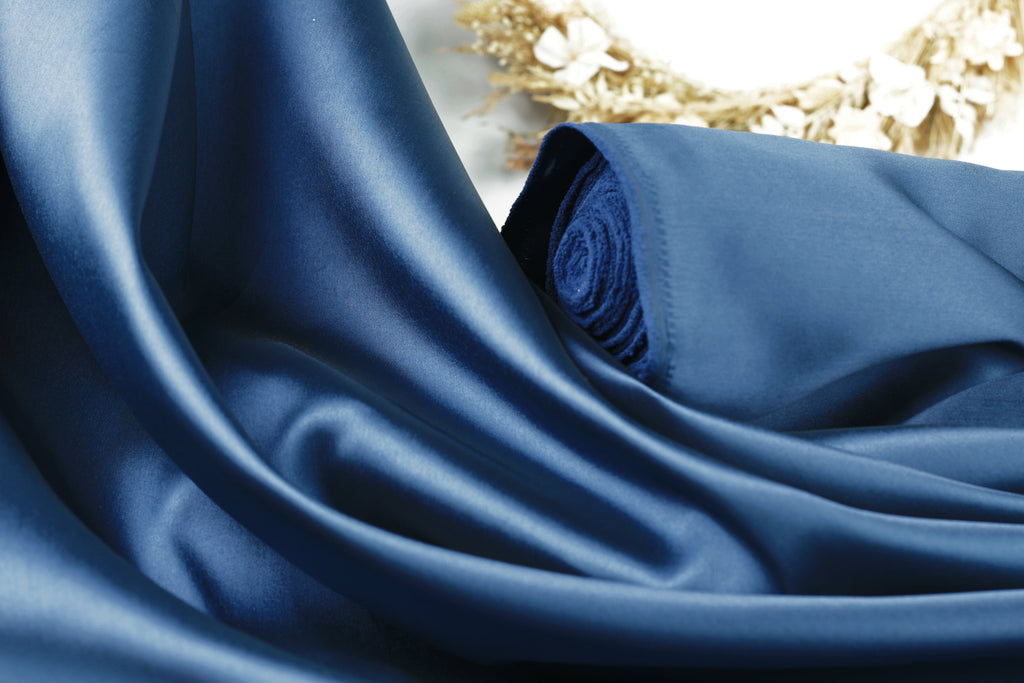 a close-up view of a blue satin fabric, with a blurred floral background.