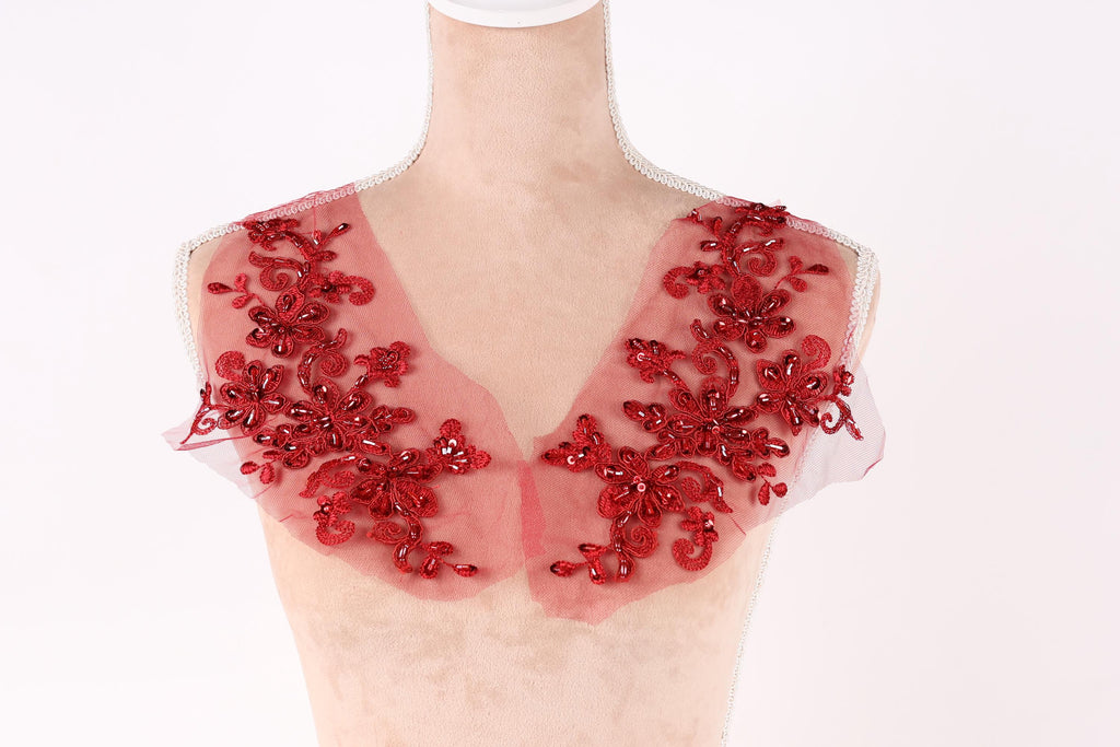 A mannequin wearing a red, sheer collar with intricate floral embroidery.