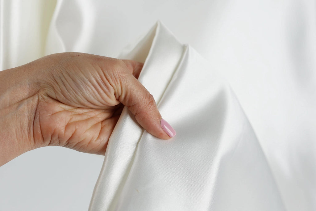 A hand is holding a white fabric, possibly a piece of clothing or a textile, with a pink nail polish on the fingernail.