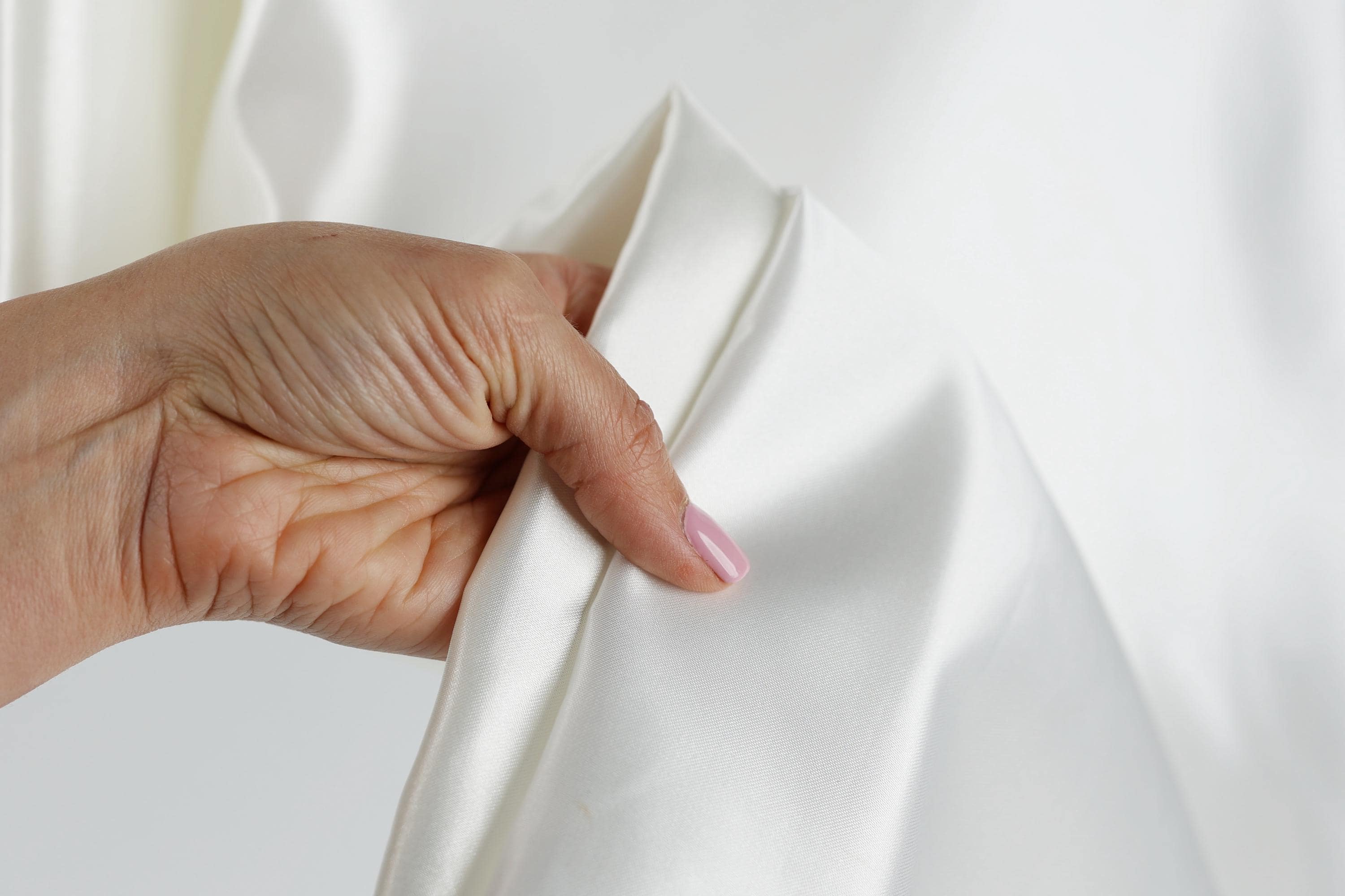 A hand is holding a white fabric, possibly a piece of clothing or a textile, with a pink nail polish on the fingernail.