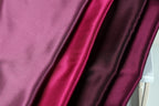 a close-up view of a fabric with three distinct colors: pink, red, and purple. The fabric appears to be a type of satin or silk material, with a shiny and smooth texture.