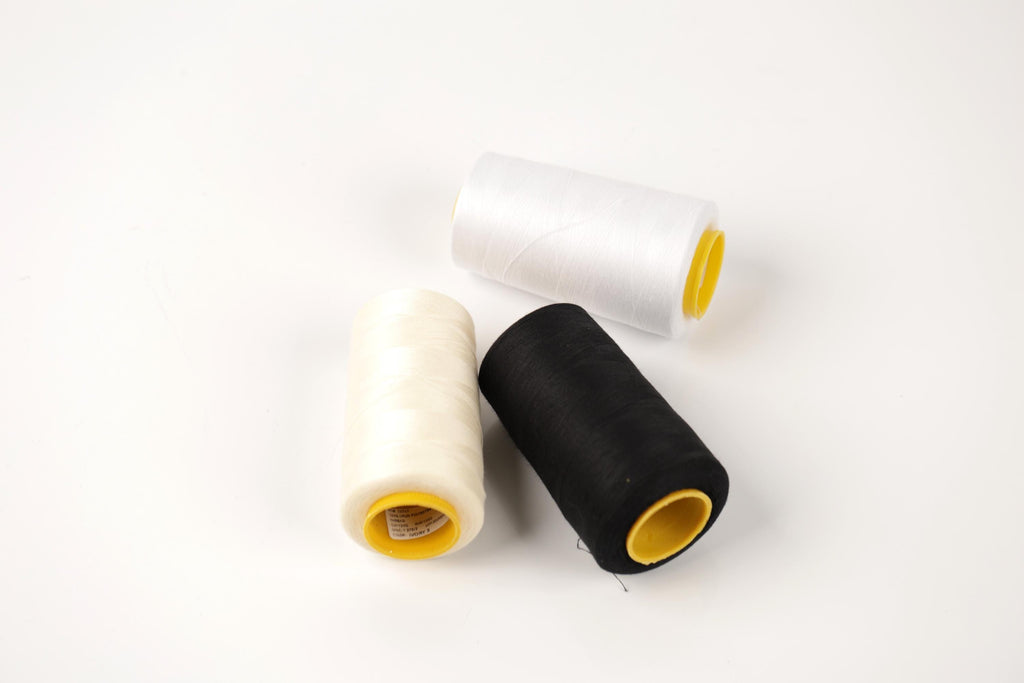three spools of thread, including white, black, and yellow, arranged on a white background.